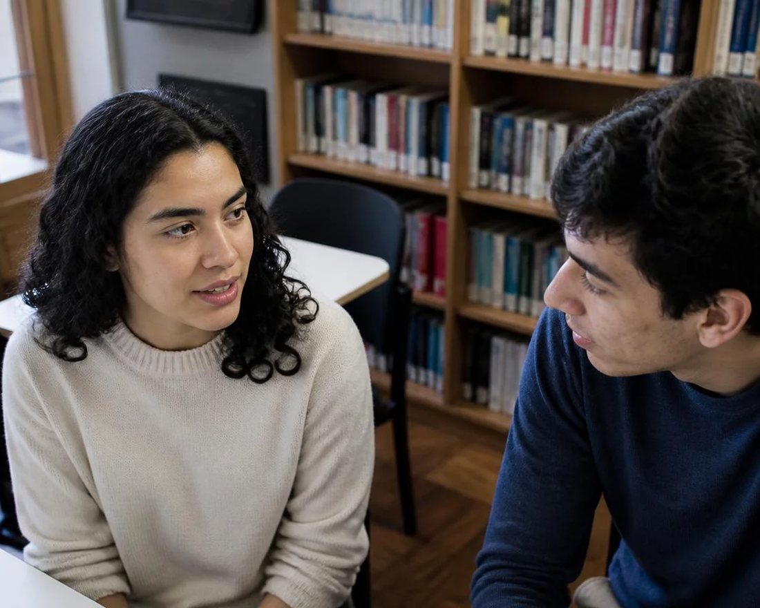 Dois participantes sentados de frente um para o outro numa rodada de réplica, na sala da escola no Santos